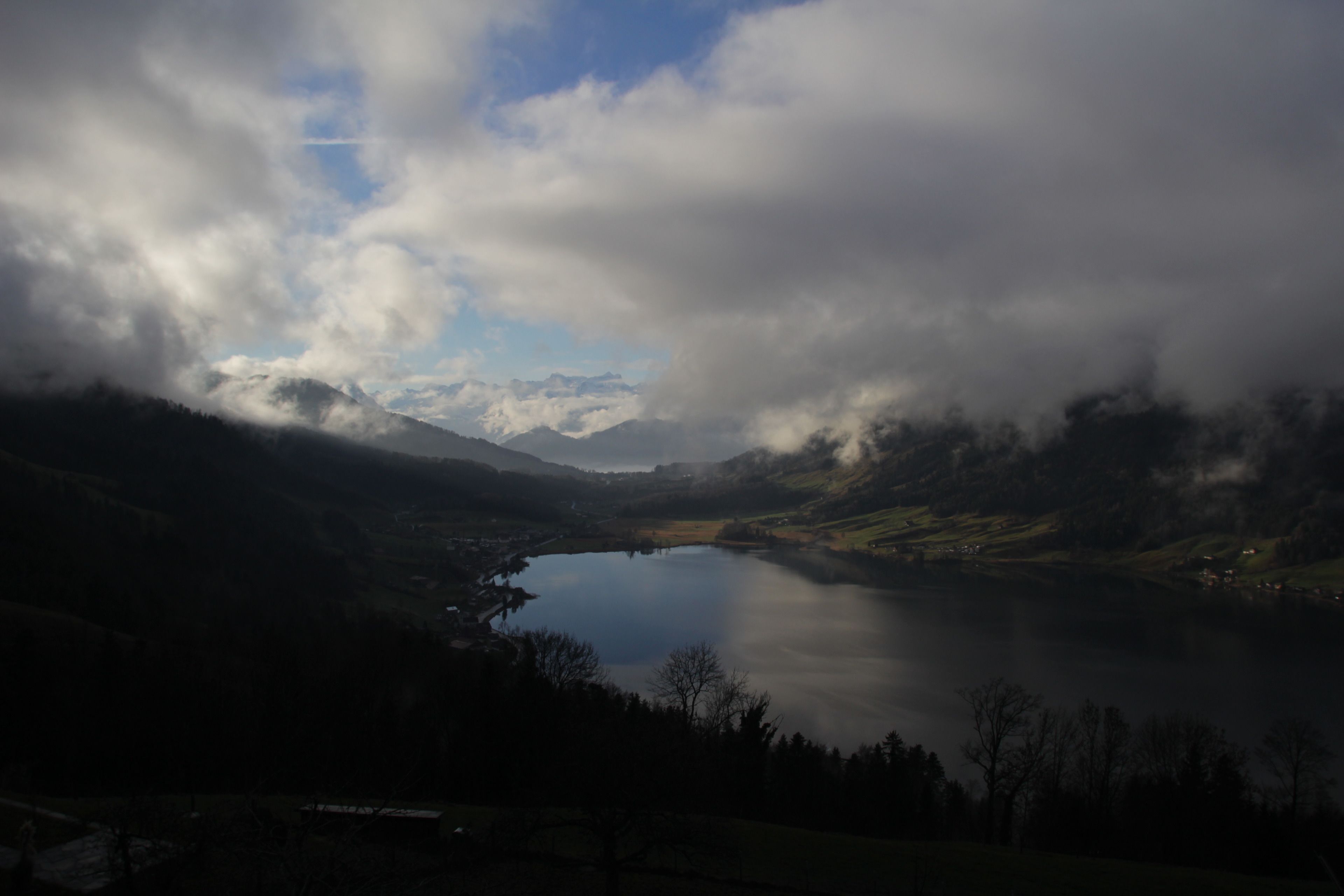 A panoramic view of a lake surrounded by mountains and clouds.