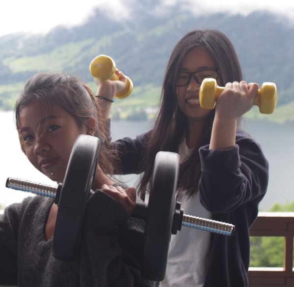Two individuals exercising with dumbbells near a body of water with a mountainous backdrop. - The Outdoor Retreat (Oberaegeri)