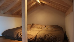Un dormitorio con techo inclinado, vigas de madera, una cama con edredón marrón y suelo de madera.