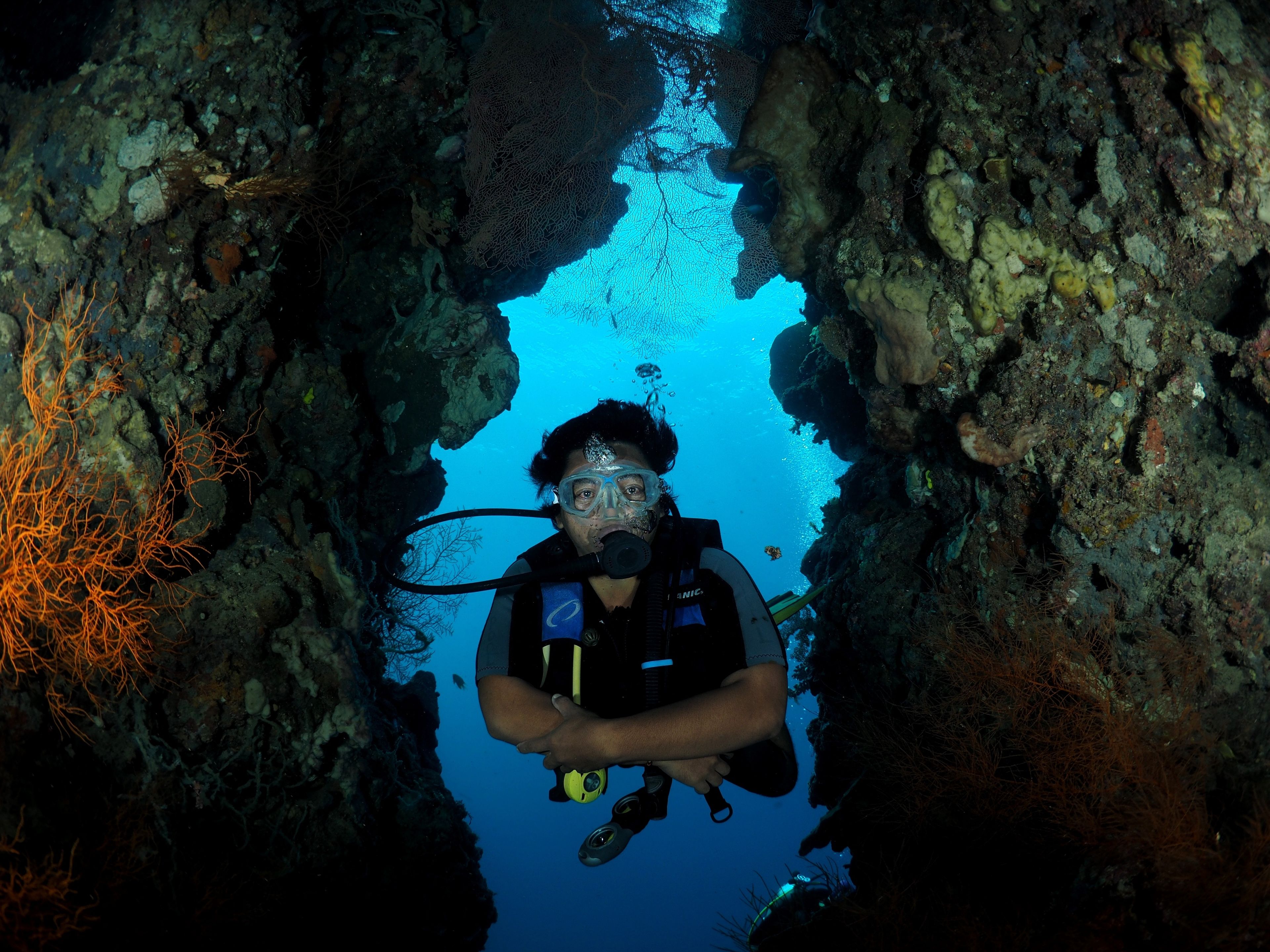 A diver in a cave with rocky walls and coral formations.