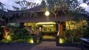 A building entrance with a covered patio area, outdoor seating, and a decorative tree.
