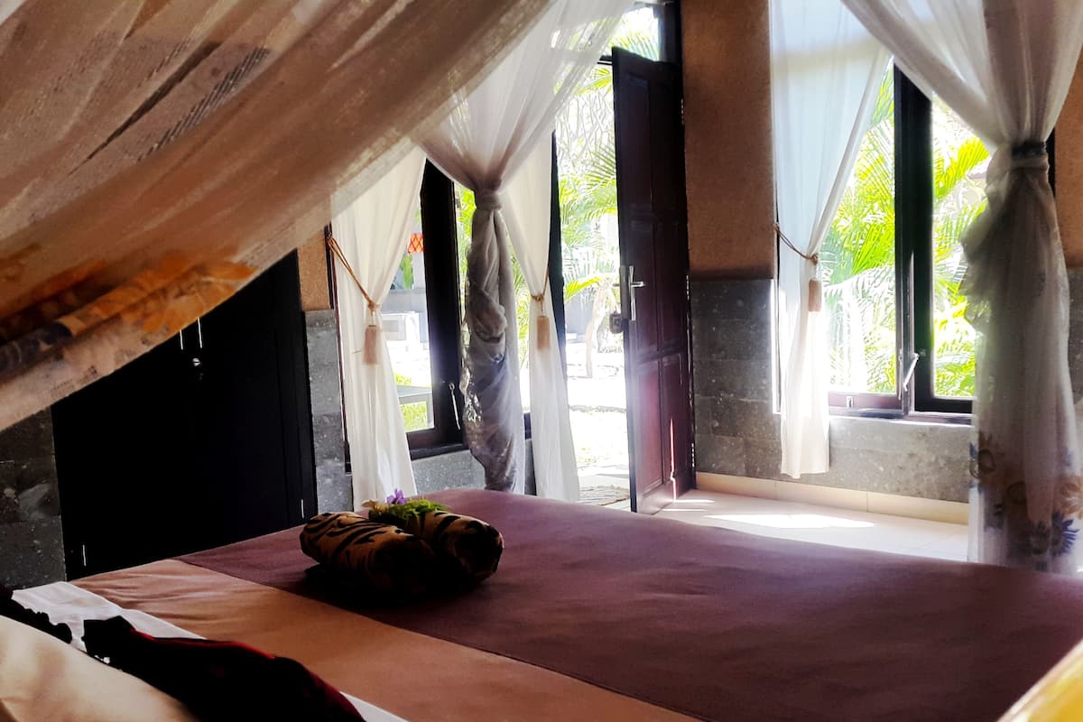 A room with a bed, curtains, and a view of greenery outside.