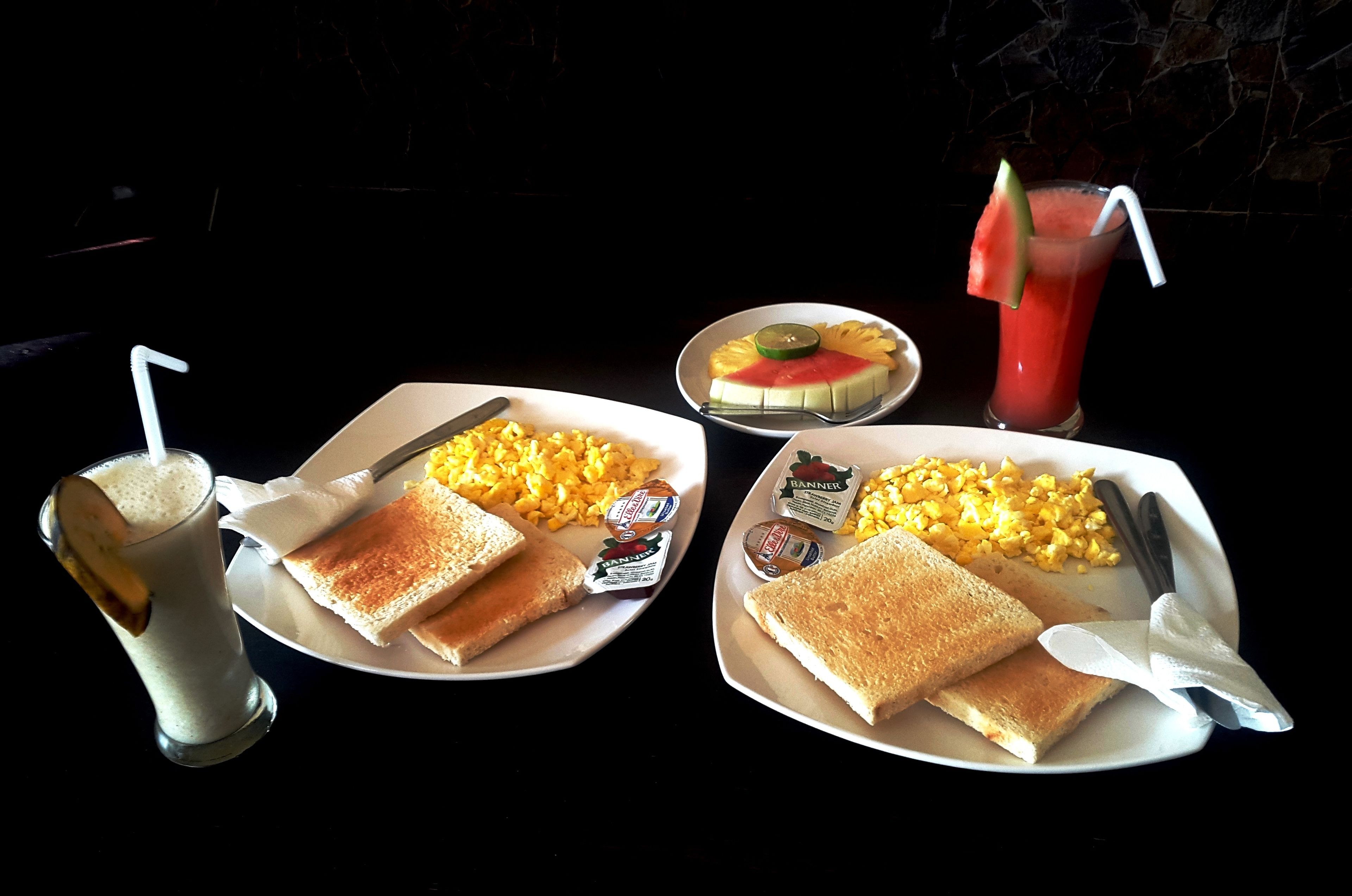 Two plates with toast, corn, and jam, a glass of milk, and a watermelon drink.