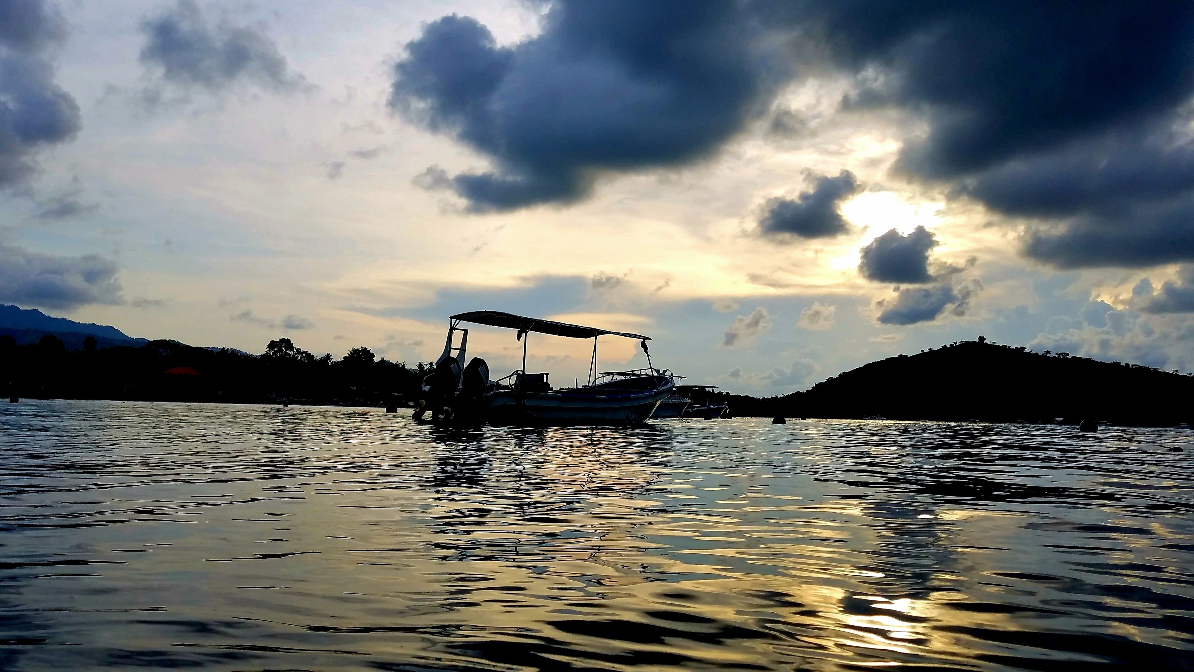 A boat docked at a calm body of water with a sunset in the background.