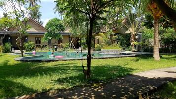 A well-maintained garden with a swimming pool, surrounded by lush greenery and palm trees.
