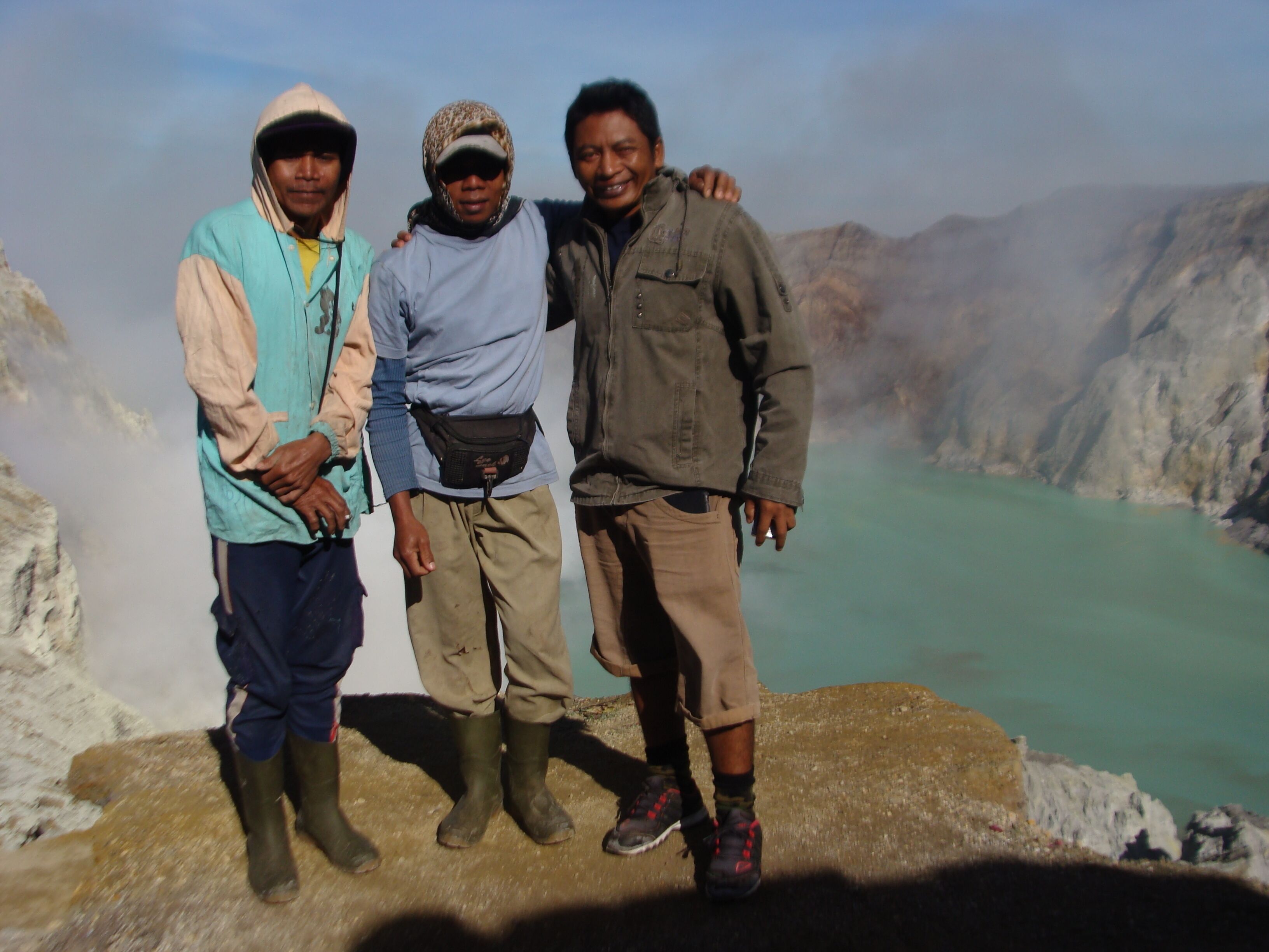 Three people standing on a rocky outcrop with a mountainous landscape in the background.