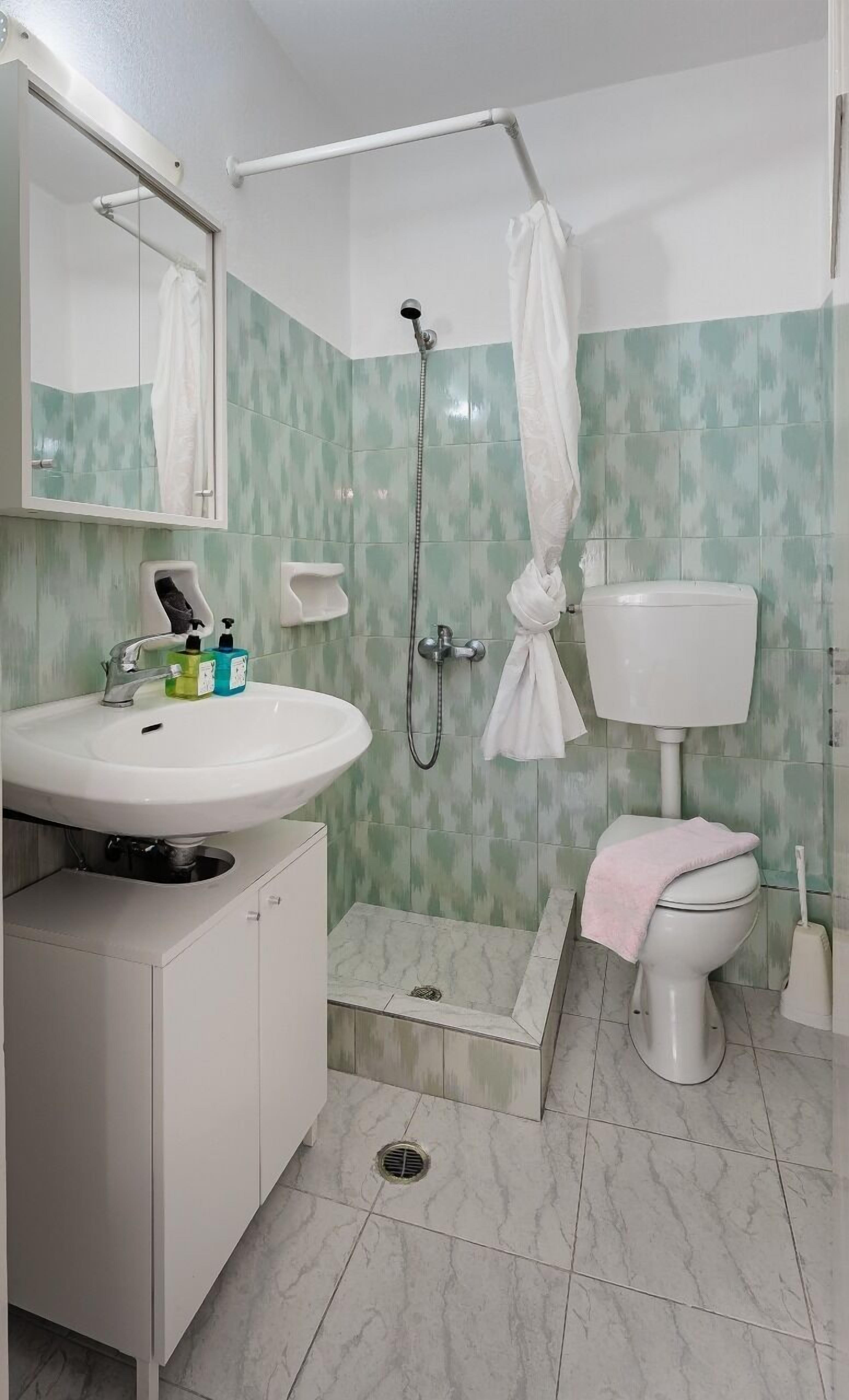 A bathroom with a sink, toilet, shower, and a mirror.