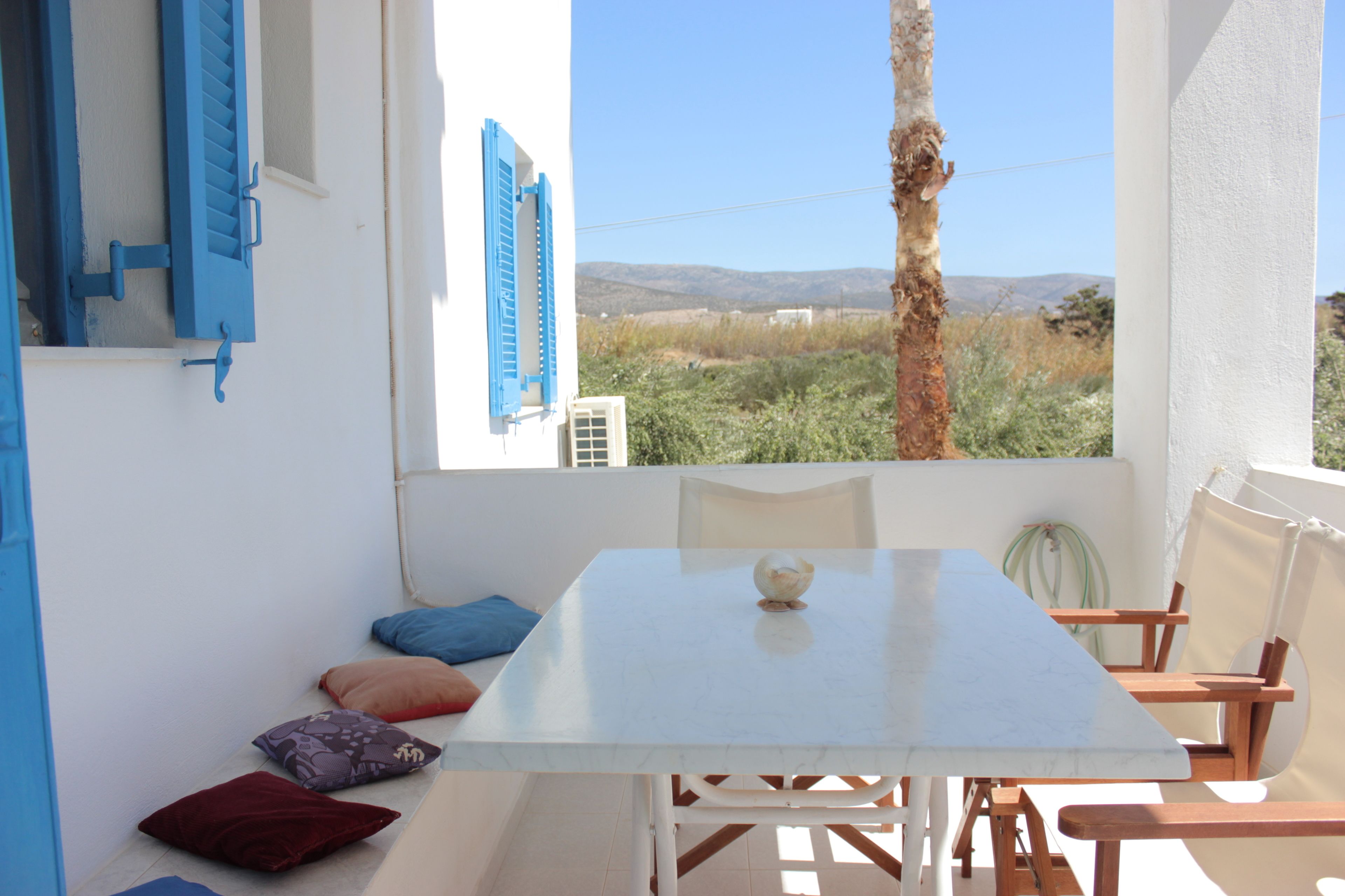 A white table with a single decorative item, blue shutters, and a view of a tree and landscape through a window.