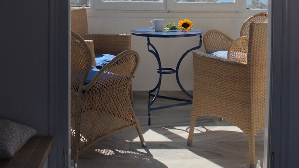 A room with wicker chairs, a small table, and a view of a lake and hills.