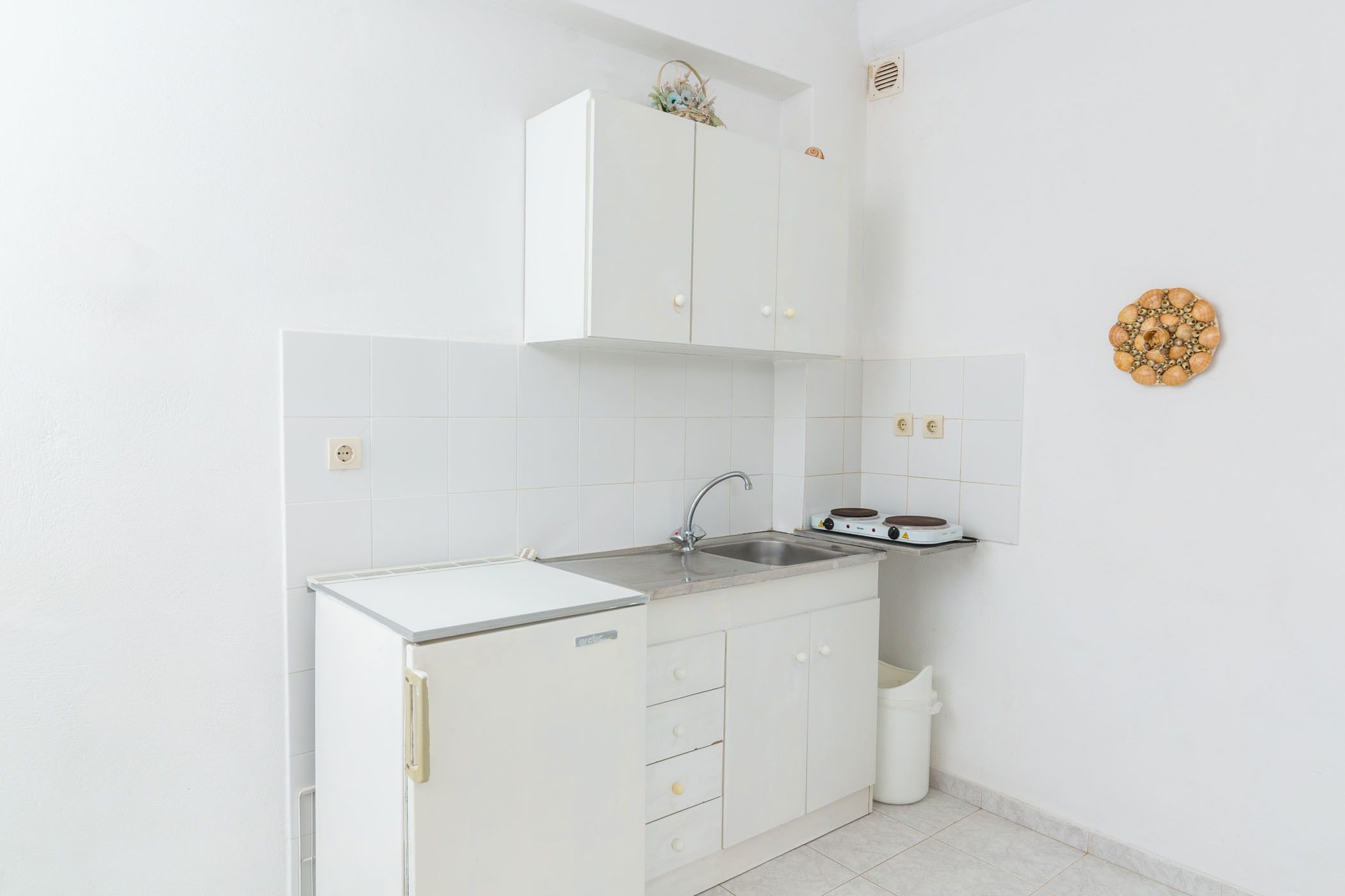 A compact kitchen with white cabinets, a stainless steel sink, and a small trash bin.