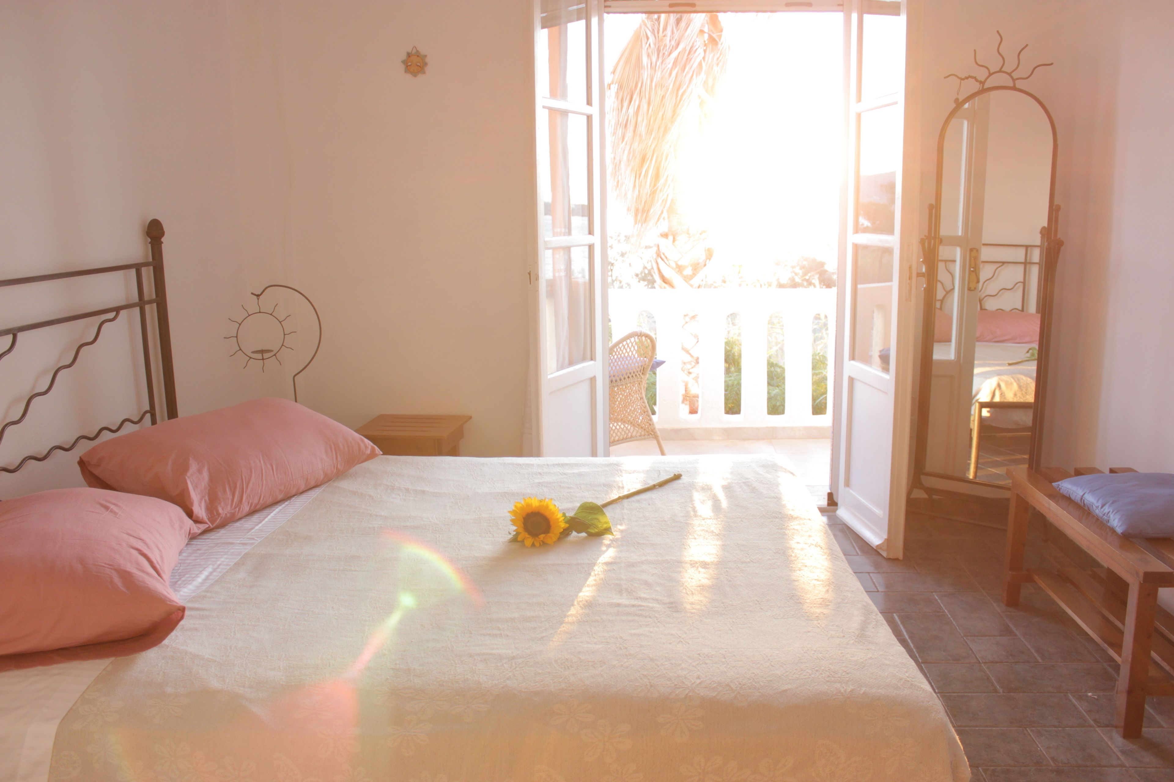 A bedroom with a bed, pillows, a sunflowers decoration, a mirror, and a balcony view.