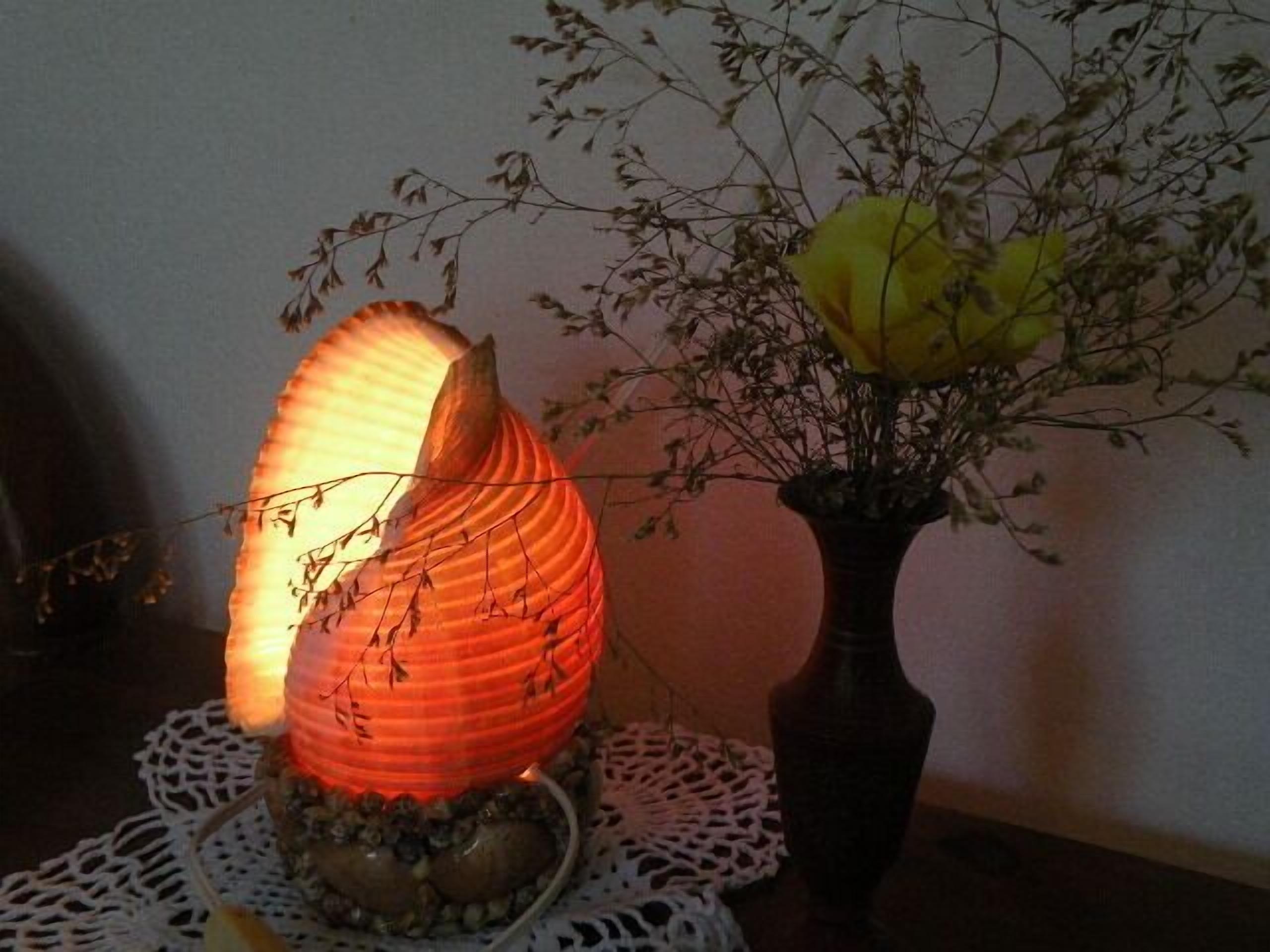 A decorative lamp with a unique design, placed on a table with a lace doily and a vase with dried flowers.