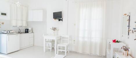 A white room with a bed, a desk, a chair, a TV, and a kitchenette.