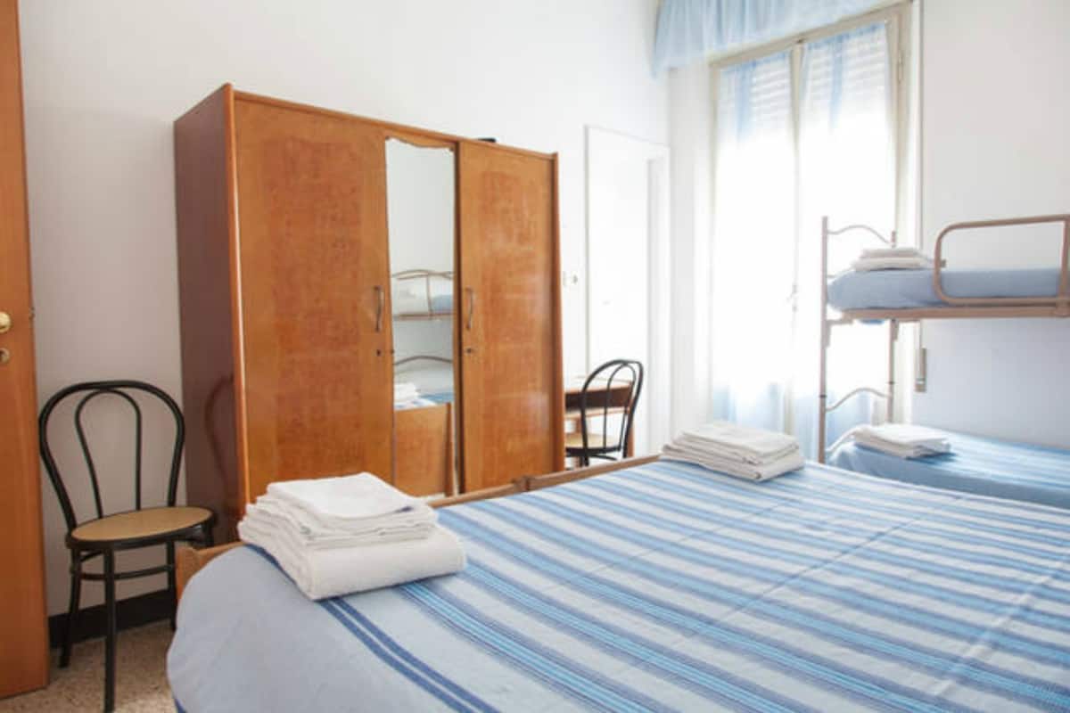 A bedroom with a bunk bed, a wooden wardrobe, a chair, and a window with curtains.