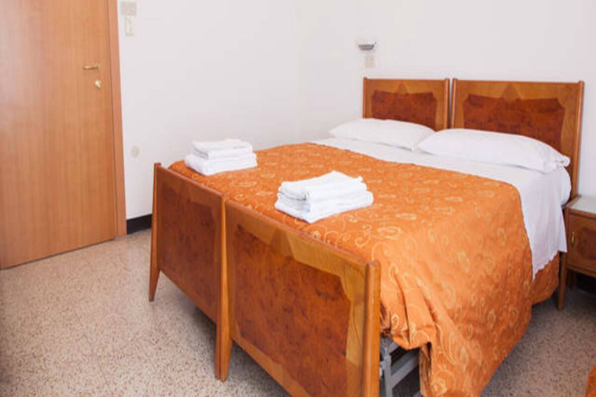 A single-bed room with a wooden headboard, a wooden wardrobe, and a white wall with a small notice.