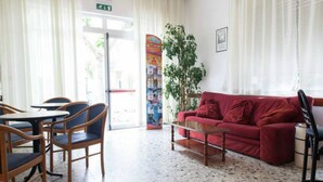 A room with a red sofa, wooden chairs, a small table, and a plant. - Hotel Ronconi (Rimini)