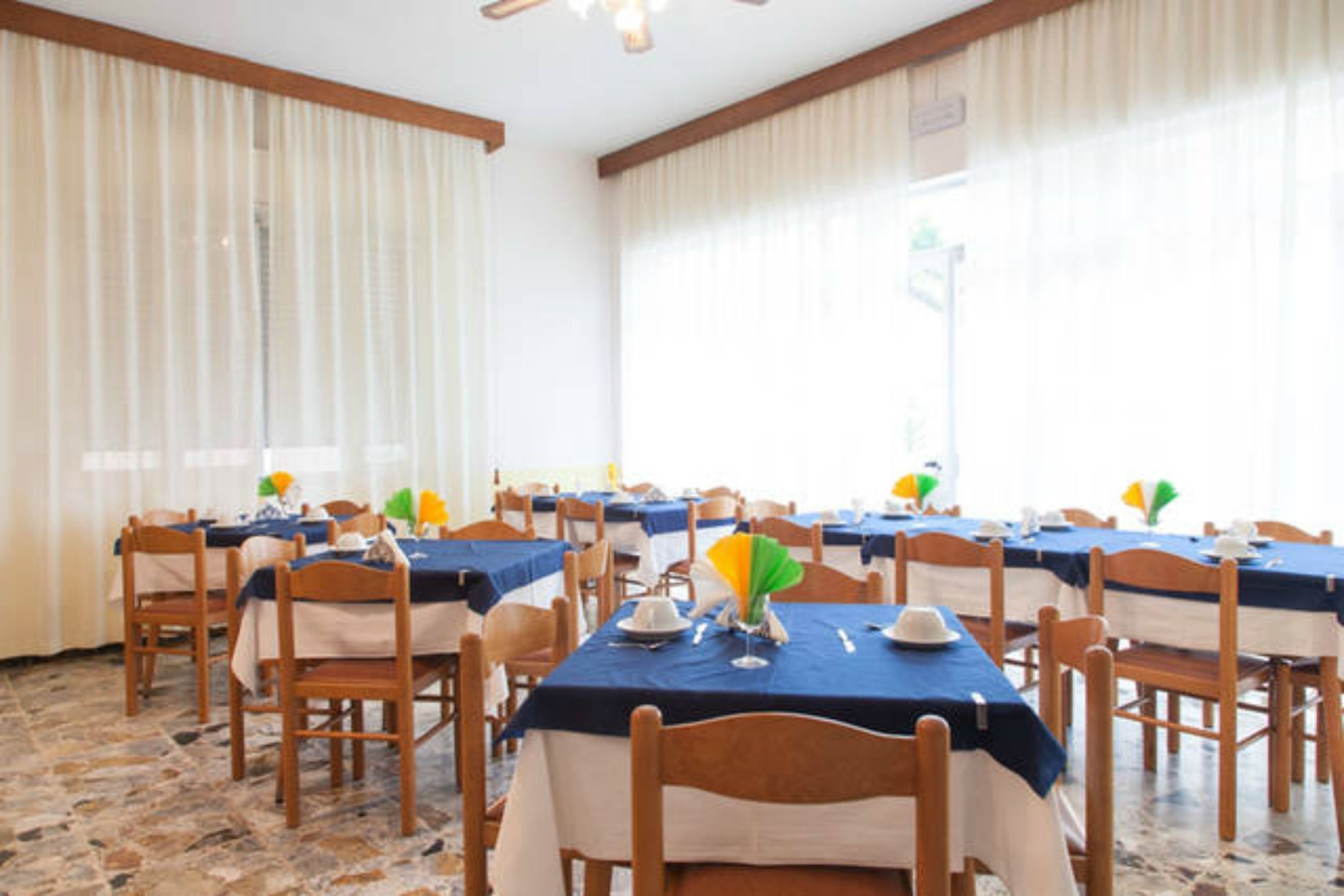 A dining area with tables set for a meal, wooden chairs, and a stone floor.