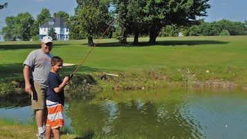 A man and a boy fishing by a pond with a house in the background.