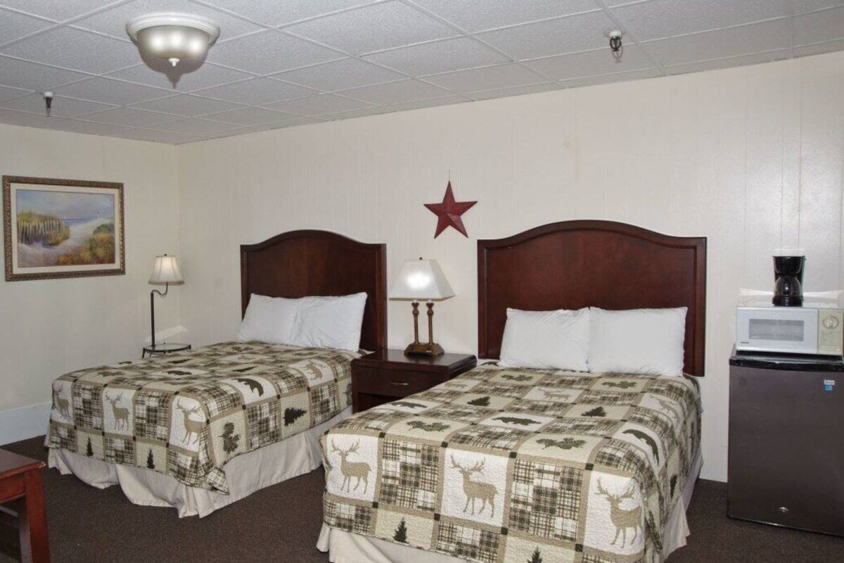 A hotel room with two beds, each with a quilted deer pattern, a star decoration on the wall, a painting, and a coffee maker.