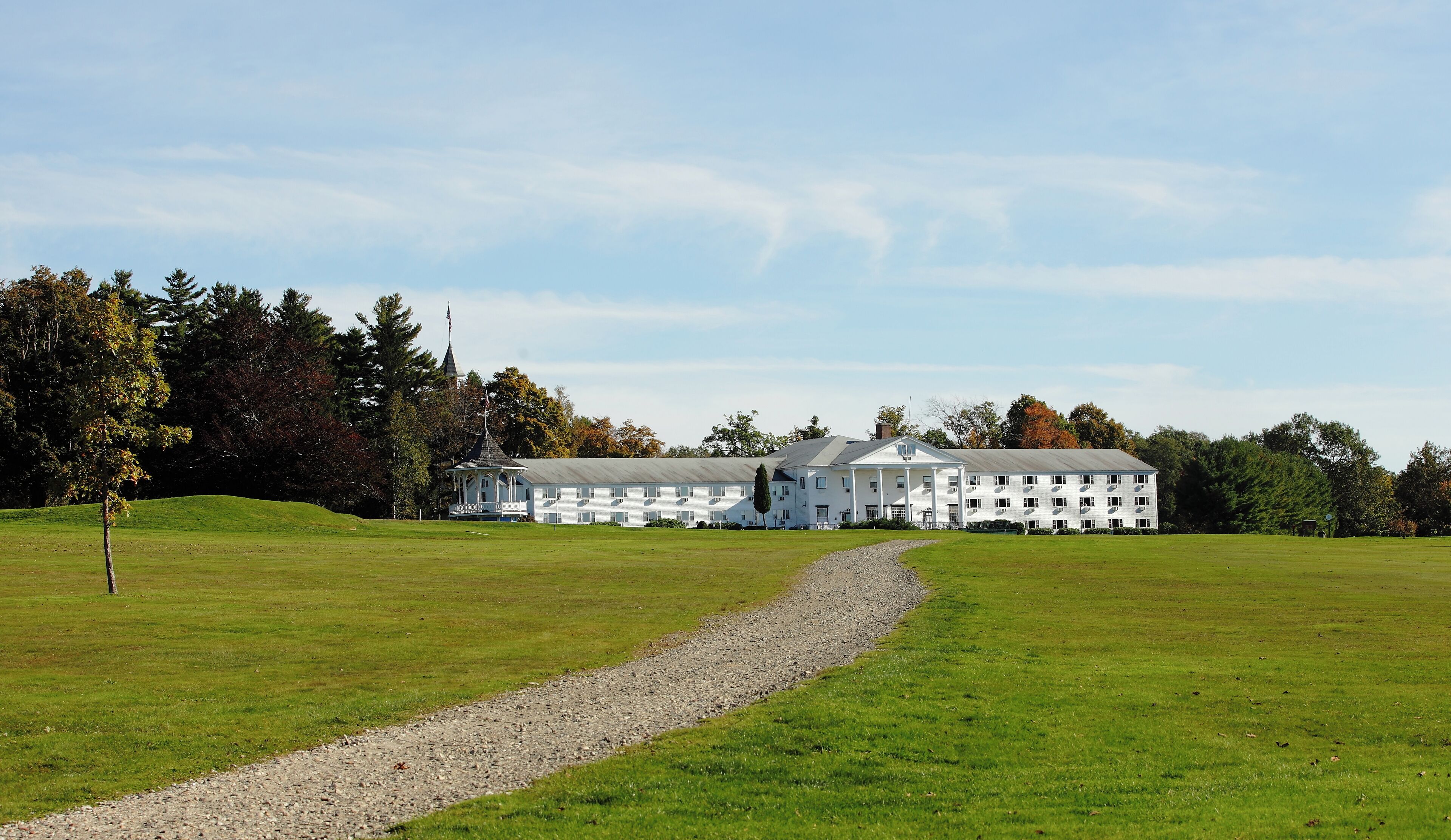A large white building with multiple windows and a central tower, surrounded by a well-maintained lawn and trees.