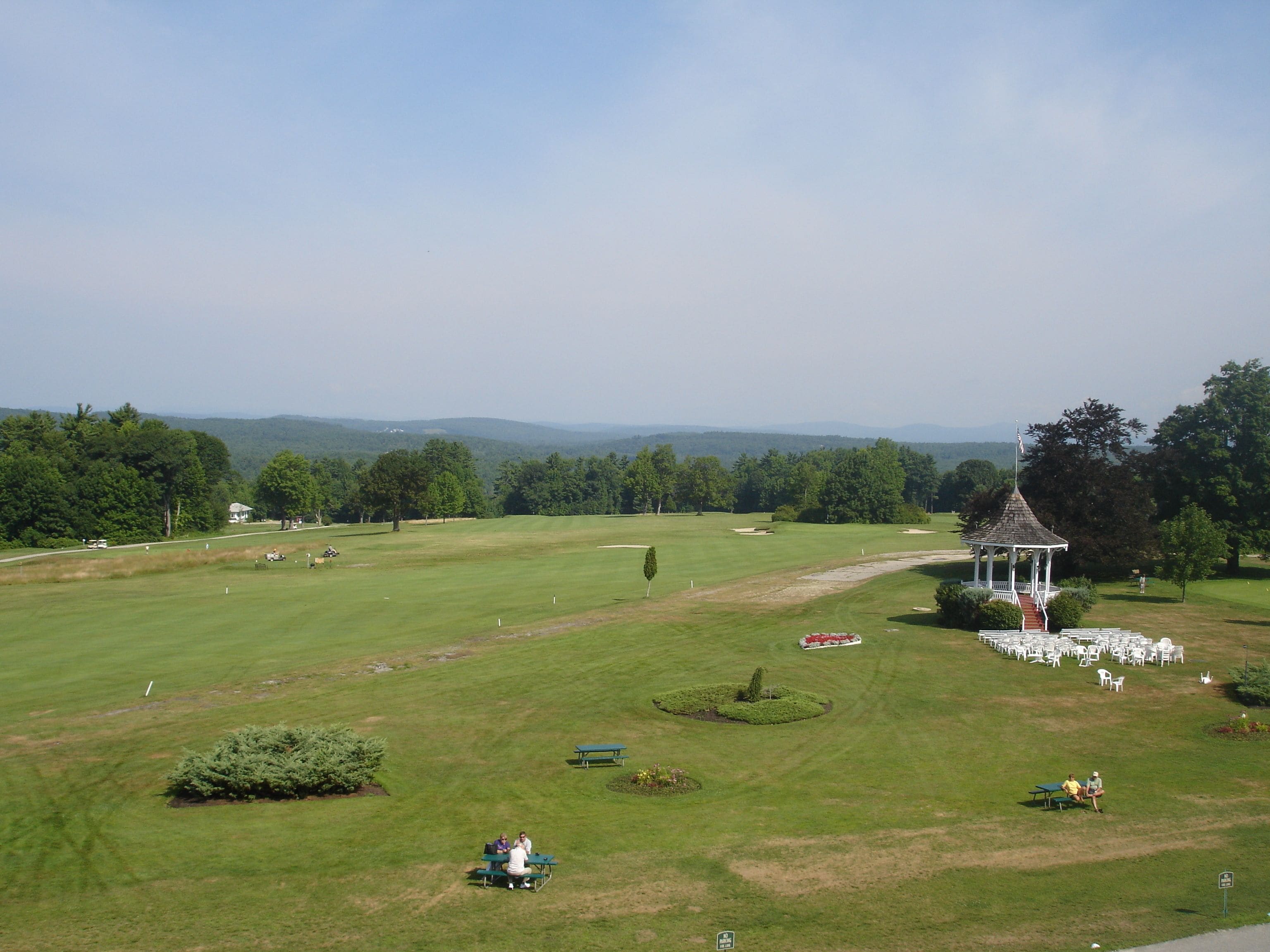 A golf course with a gazebo, picnic tables, and a flagpole.