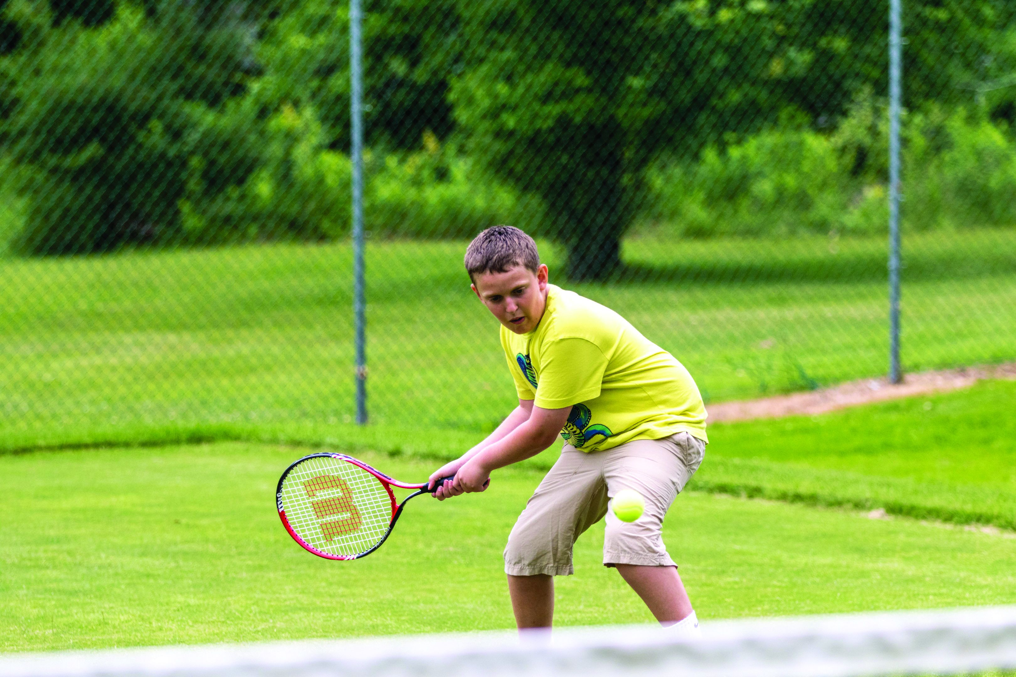 Un court de tennis où un joueur, vêtu d’un maillot jaune et d’un short beige, se prépare à frapper une balle de tennis.