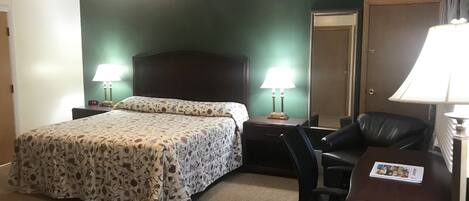 A hotel room with a bed, two bedside tables with lamps, a desk with a chair, and a mirror.