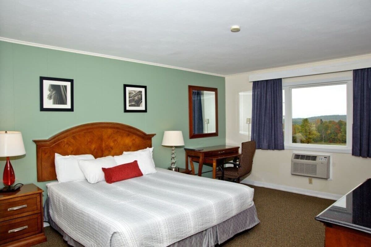 A hotel room with a large bed, a desk, a chair, and a window with curtains.