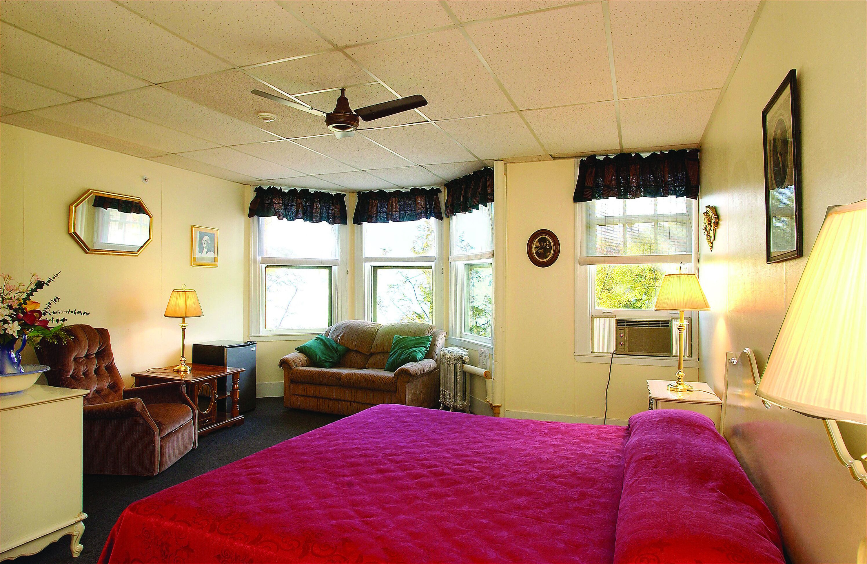 A hotel room with a large bed, a chair, a desk, a radiator, and a window with curtains.