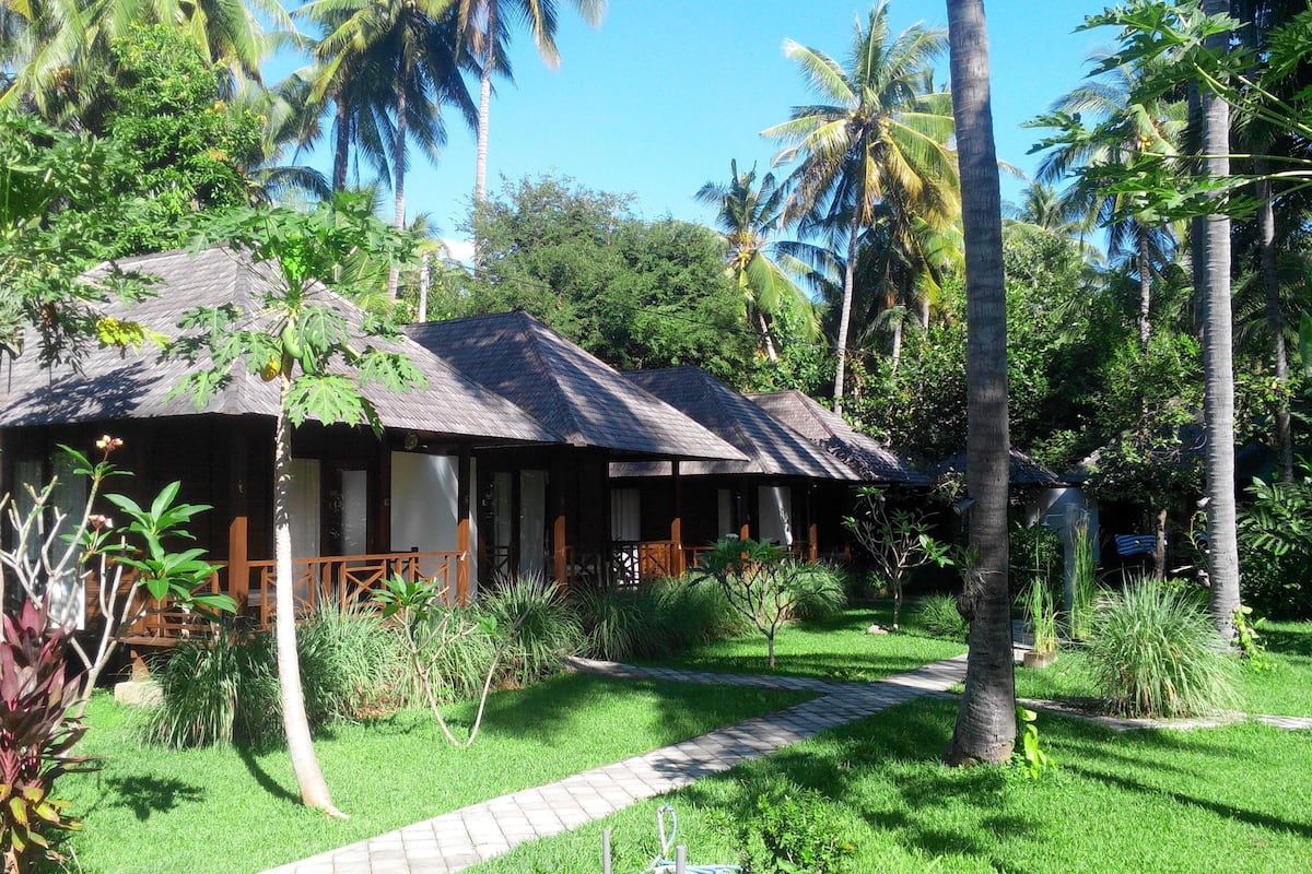 Een bungalow met rieten dak, omringd door weelderige begroeiing en palmbomen.