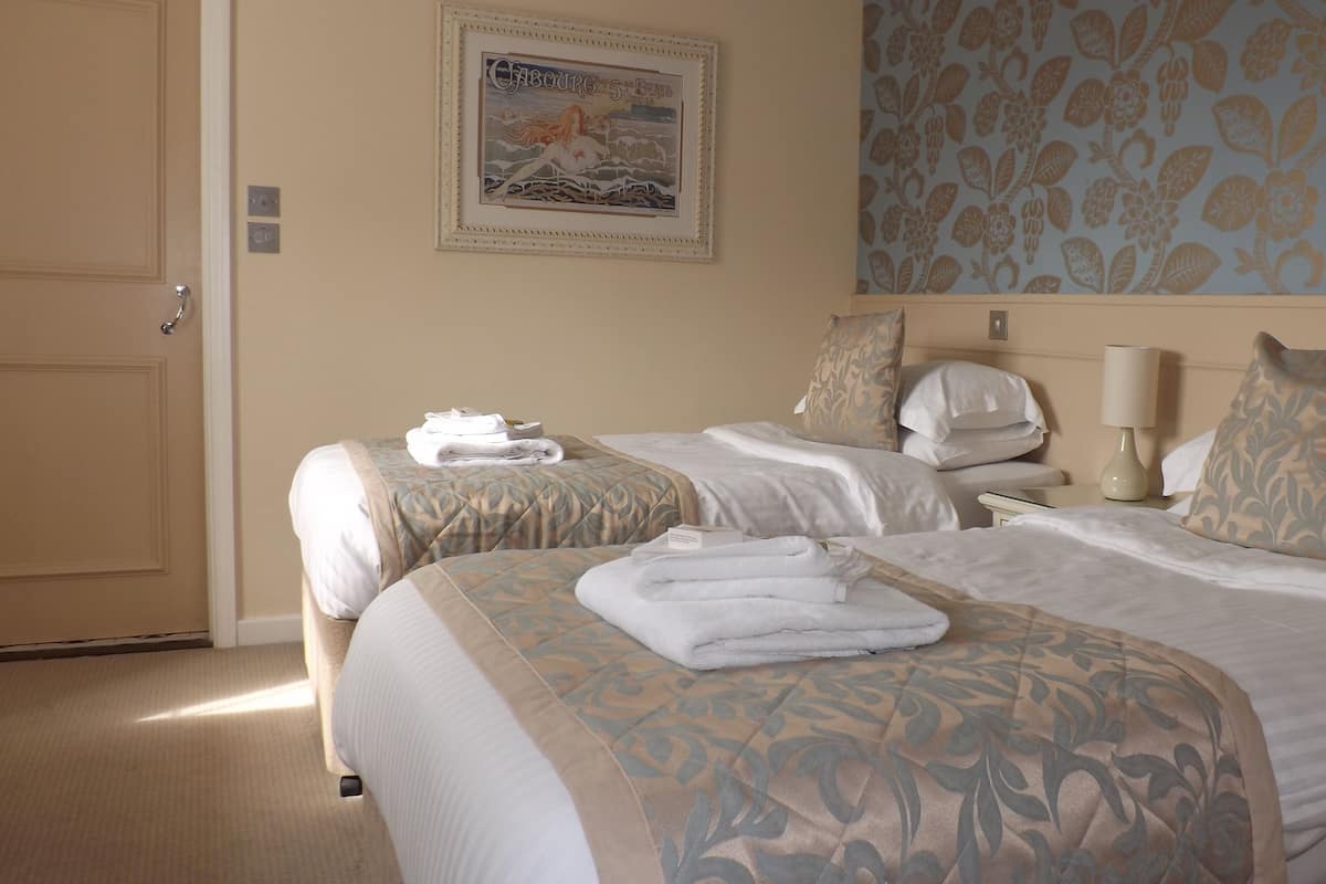 Ein Hotelzimmer mit zwei Betten, einem Bild an der Wand und einem Blumenmuster an der Tapete.