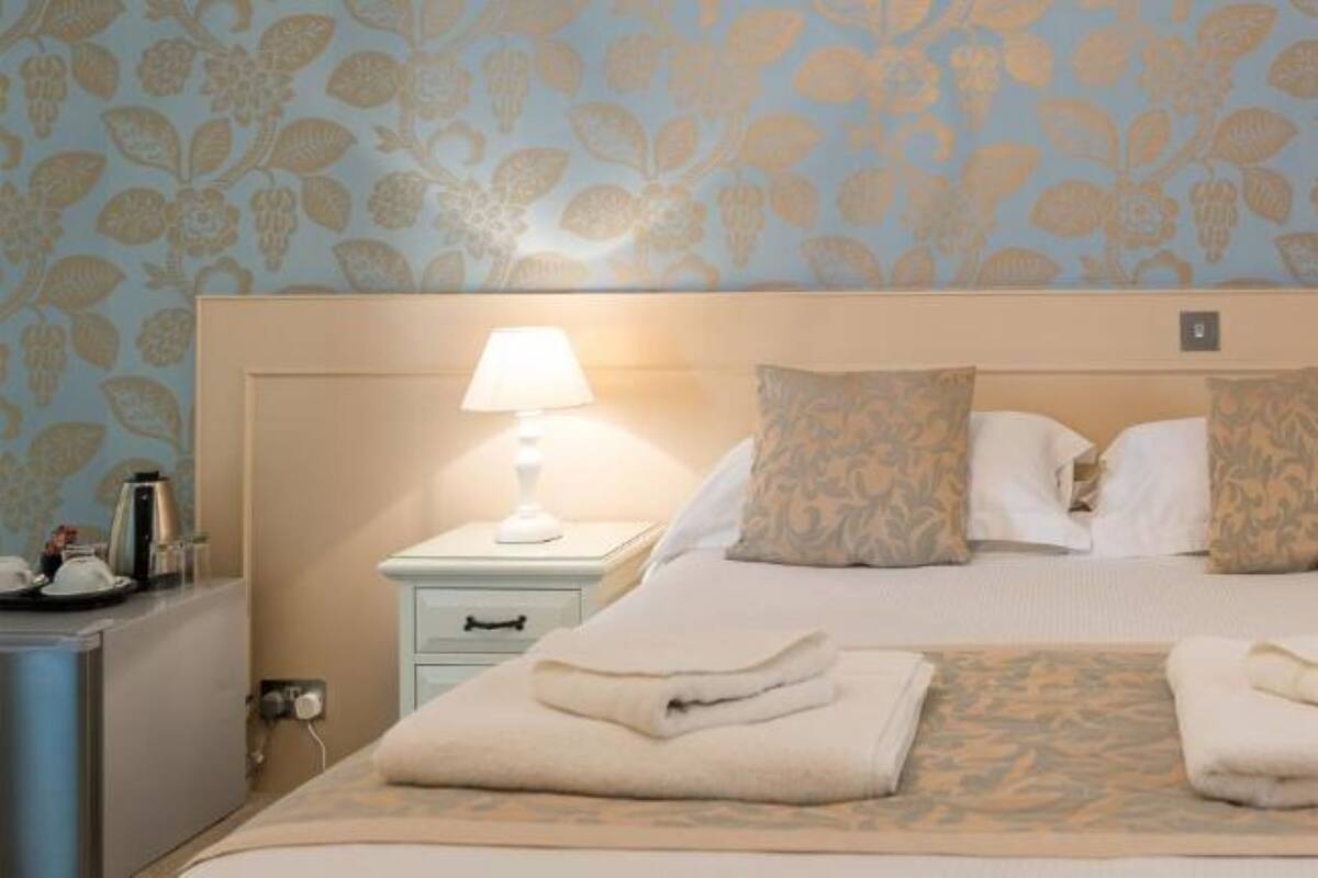Ein Hotelzimmer mit einem großen Bett, zwei Nachttischlampen, einem Nachttisch mit Kaffeemaschine und floralem Wandpapier.