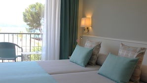 A hotel room with a bed, two pillows, a nightstand, a lamp, and a view of the outdoors. - Hotel Creta Paguera (Calvia)