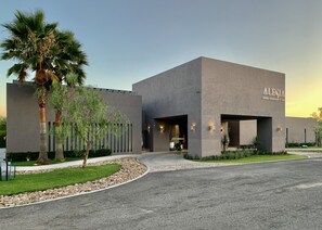 Un hotel moderno con fachada de hormigón, palmeras y un césped cuidado.