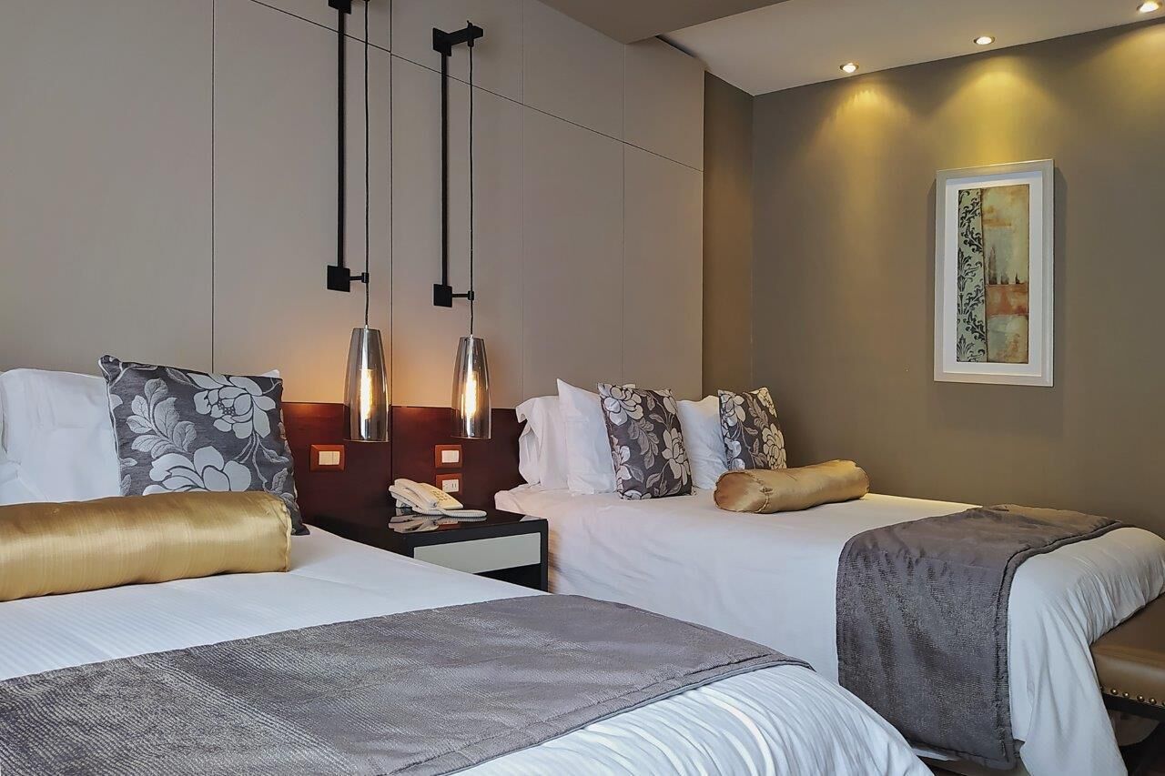 Une chambre d’hôtel avec deux lits, une table de chevet, une lampe et un tableau au mur.