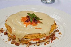 Un postre en un plato blanco con cobertura cremosa, decorado con menta y frutas secas.