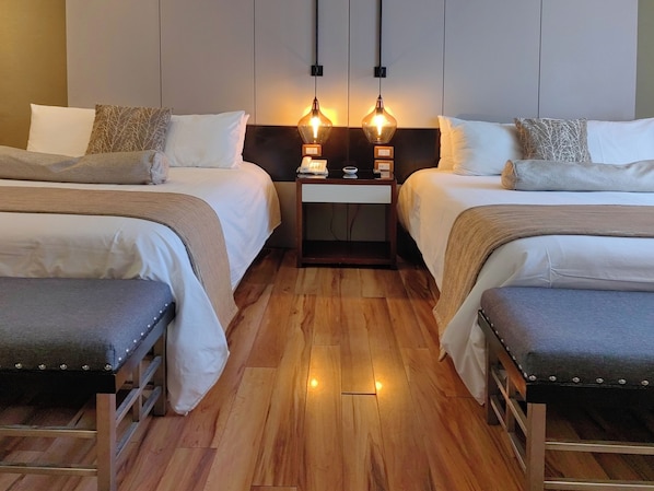 Habitación de hotel con dos camas, piso de madera y lámparas colgantes.