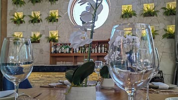 L’intérieur d’un restaurant avec une table en bois, deux verres à vin, une plante d’orchidée placée au centre et un mur en pierre orné de plantes vertes.