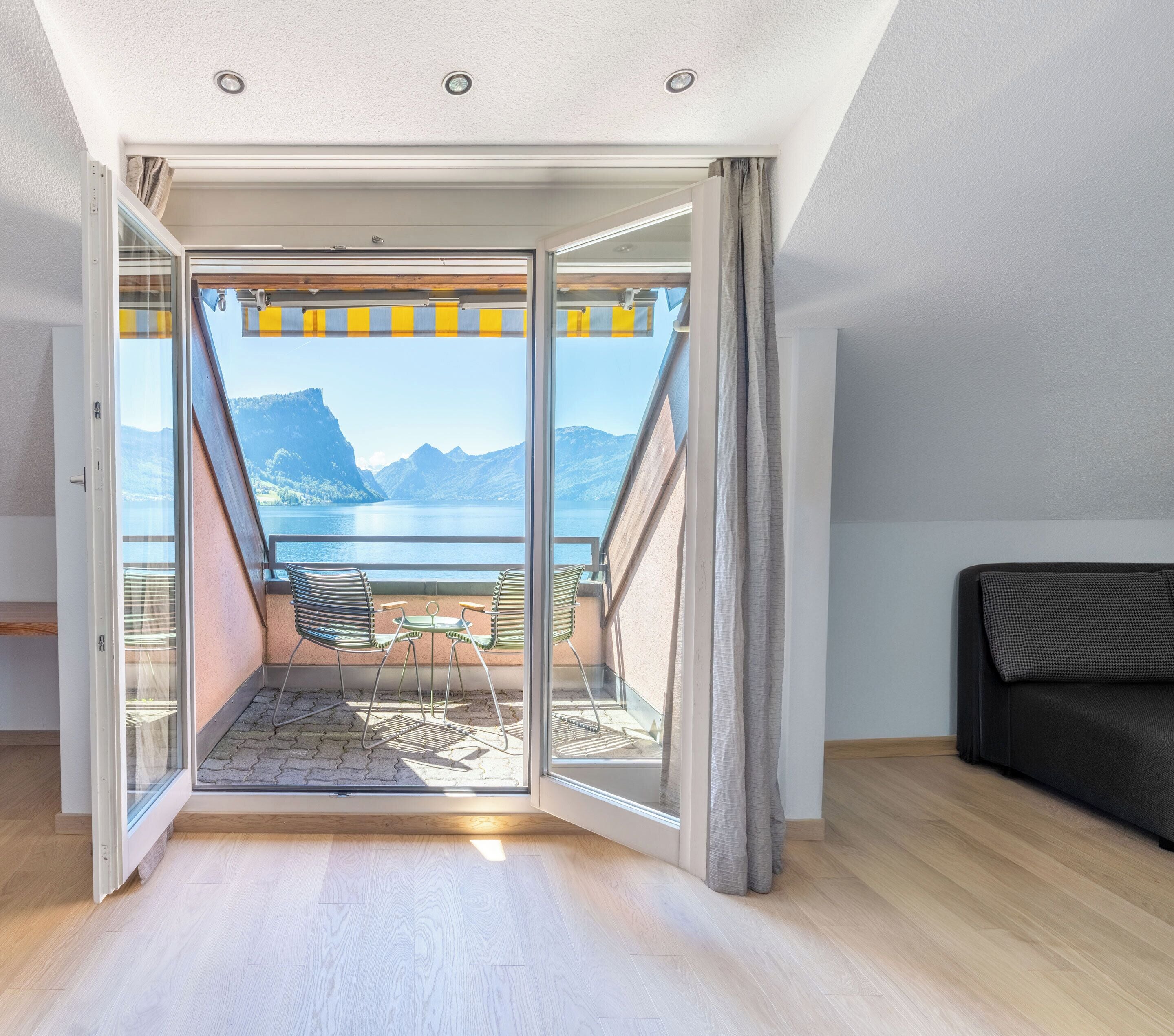 A room with a sliding glass door leading to an outdoor balcony with a view of mountains and a lake.