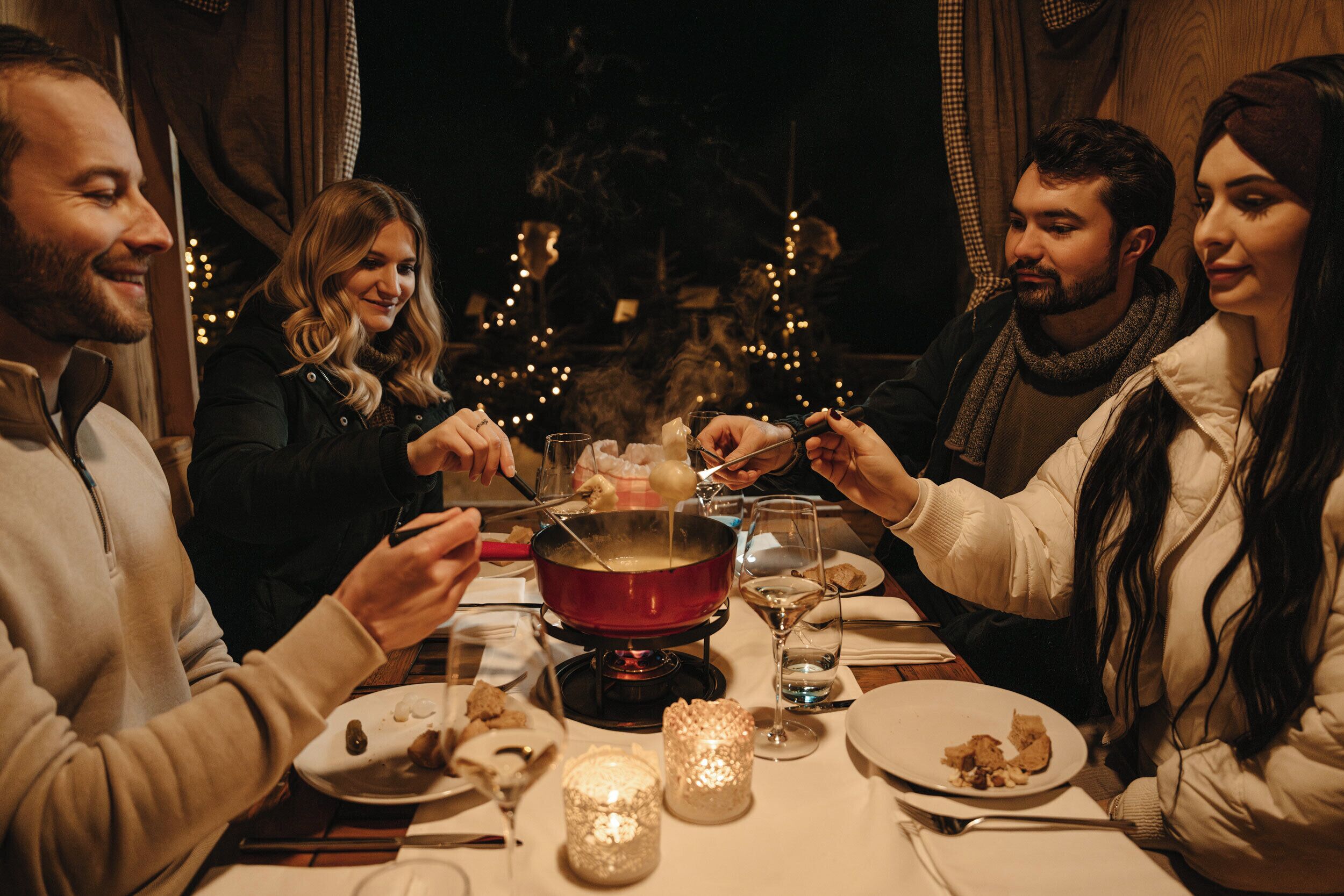 A group of people dining at a table with a fondue set, candles, and a warm ambiance.