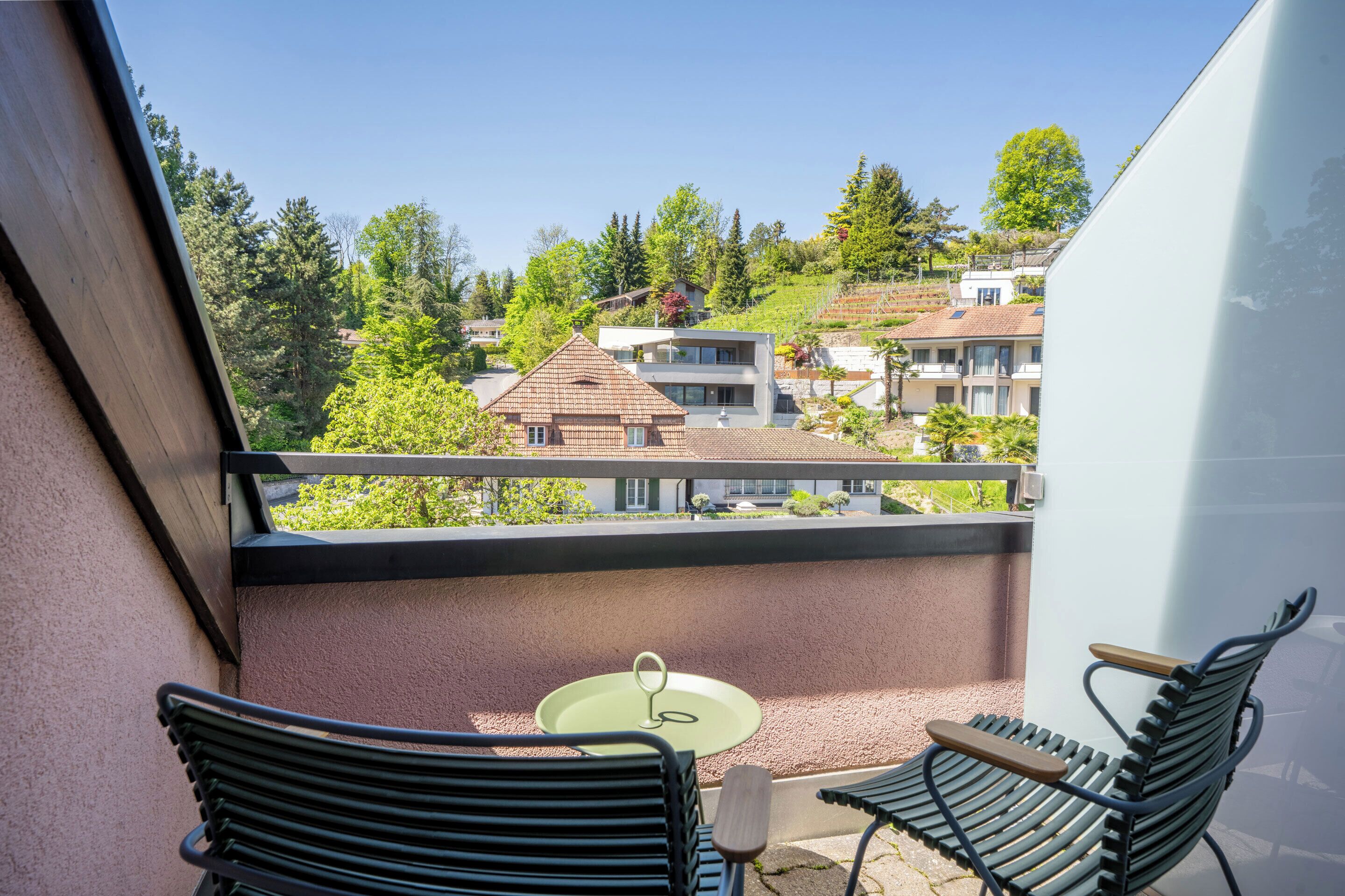Un balcón con dos sillas y una mesita, con vista a una zona residencial con casas y árboles.