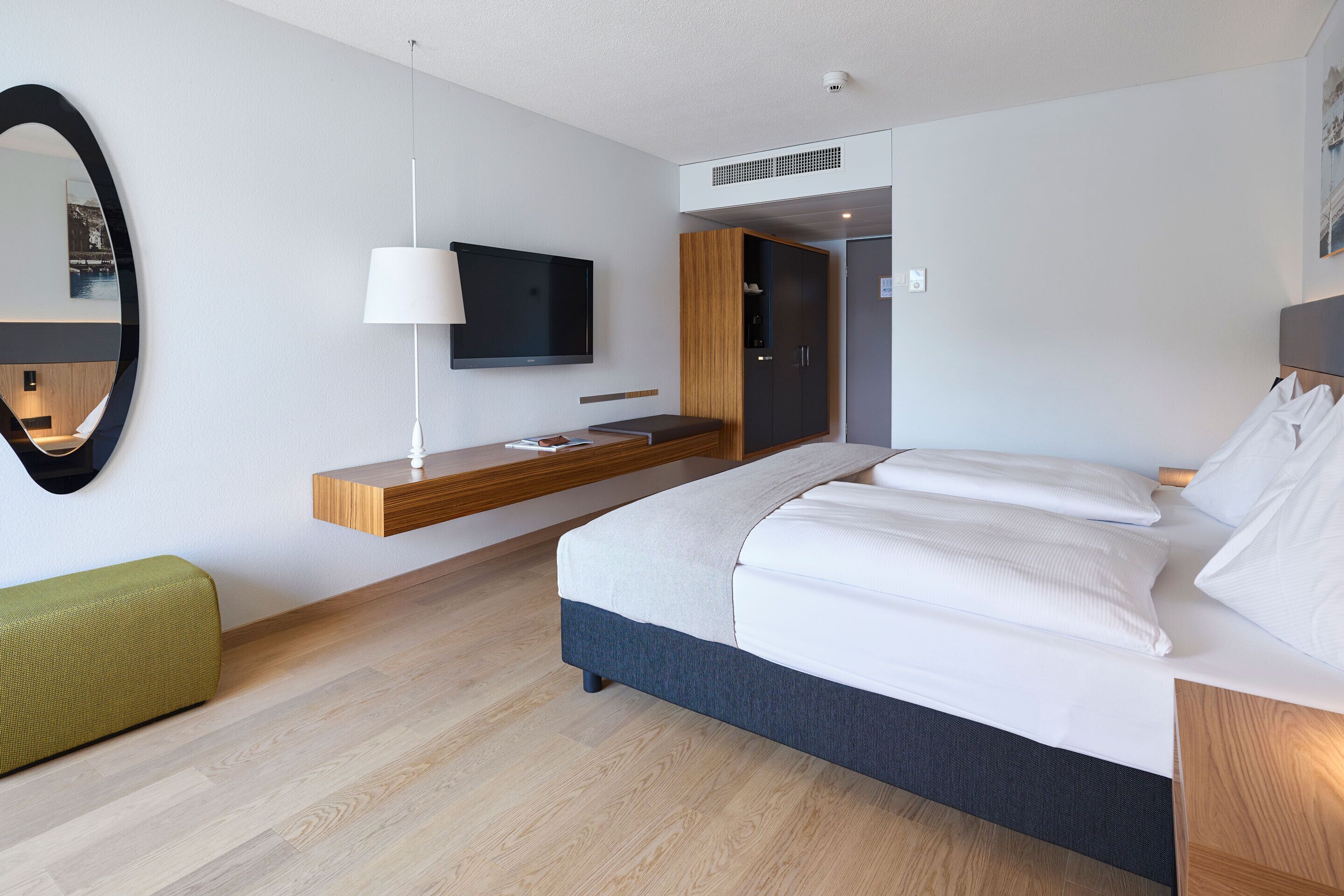 Una habitación de hotel moderna con una cama, un televisor, un espejo y un banco de madera.