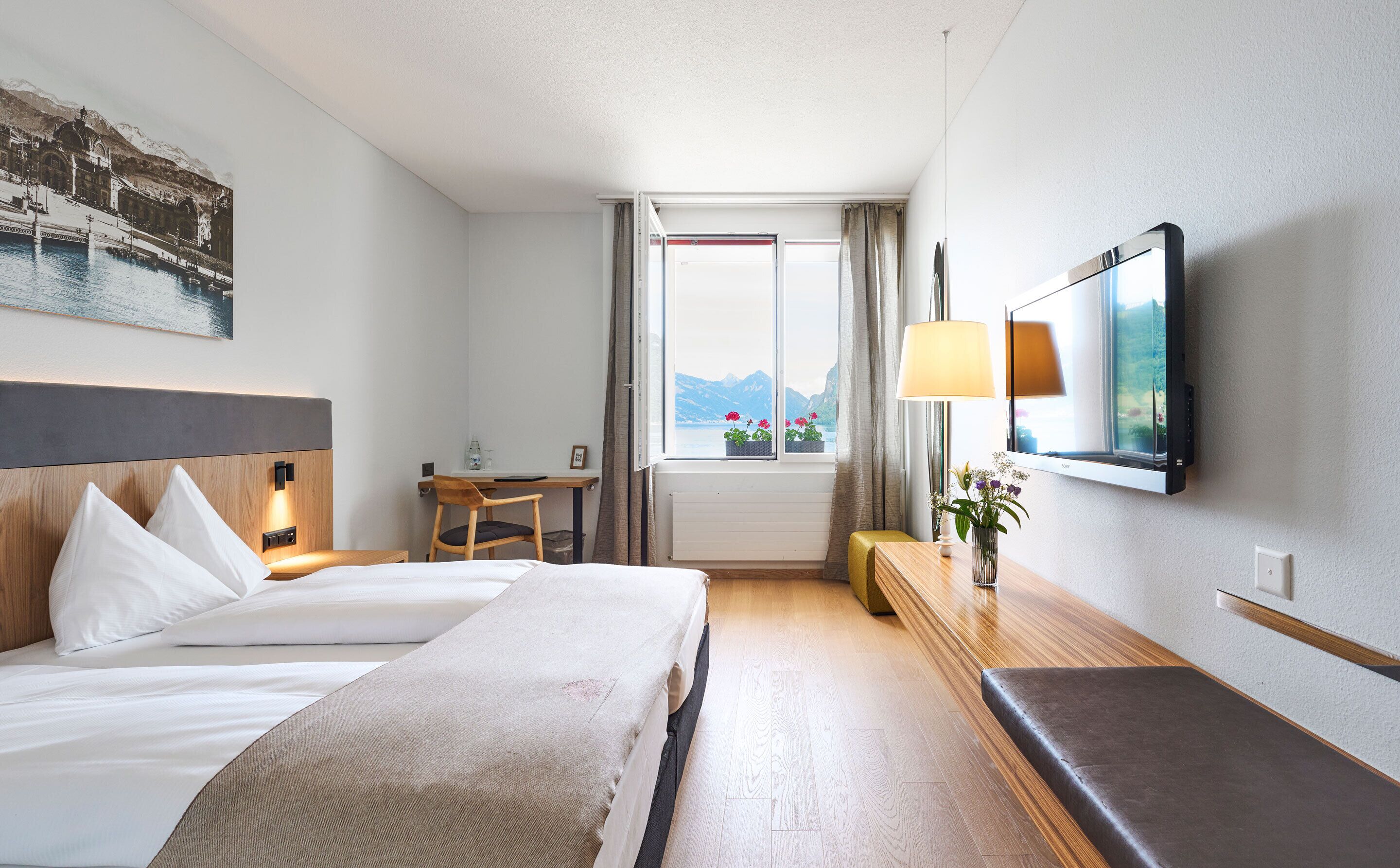 Habitación de hotel con cama, escritorio, silla, televisión y ventana con vista a la montaña.