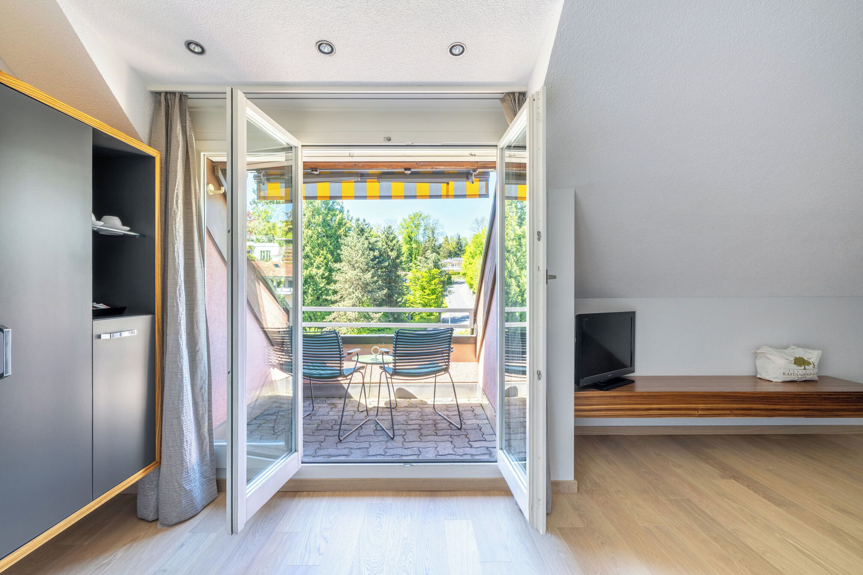 A modern living room with a sliding glass door leading to a balcony with outdoor seating.
