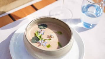 Een kom roze dessert op een wit bord, met een glas water en een wijnglas op de achtergrond.