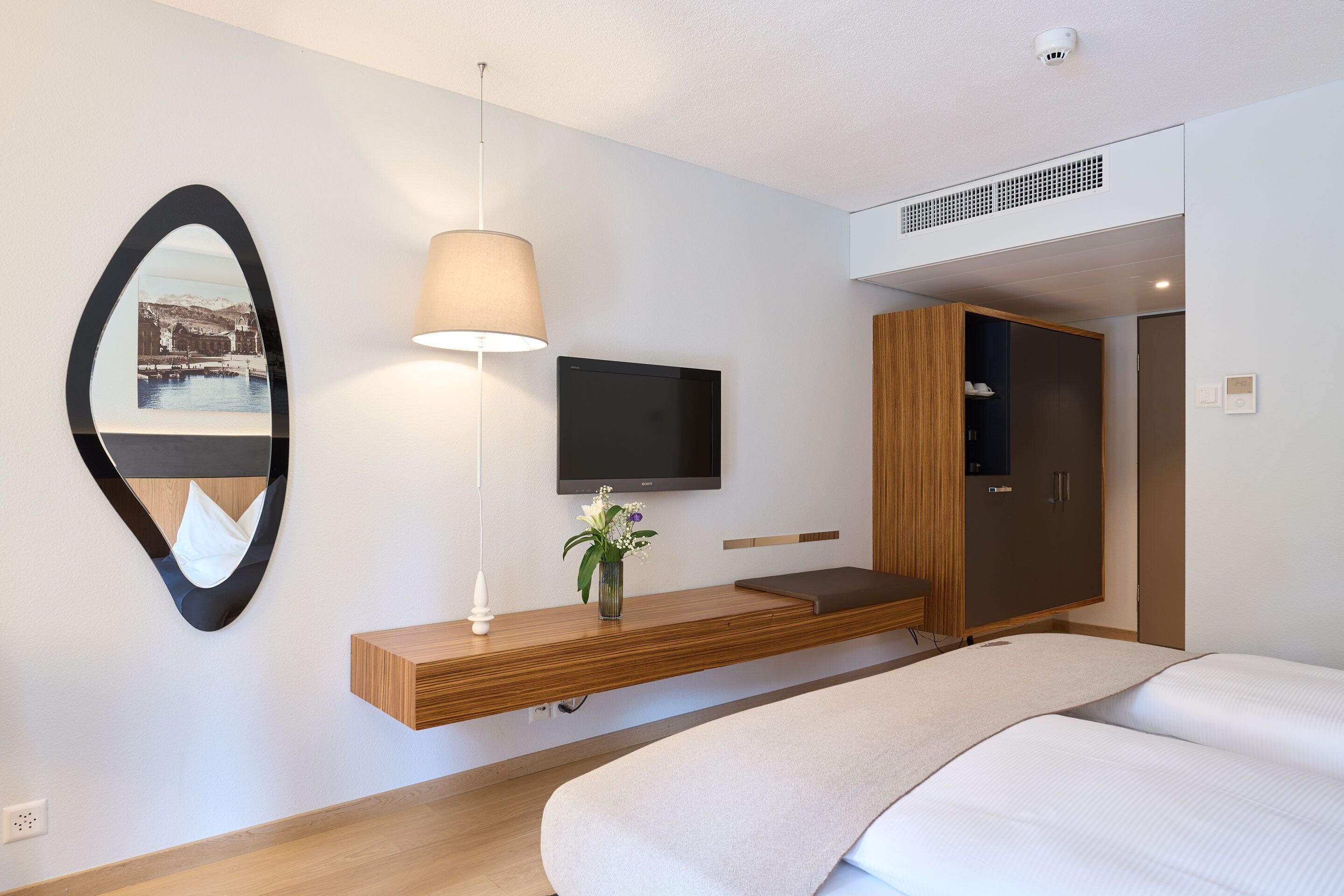 Une chambre d’hôtel moderne équipée d’un lit, d’un téléviseur fixé au mur, d’une console en bois, d’un miroir et d’une lampe.