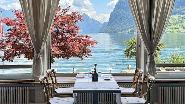 A dining area with a table set for four, facing a large window with a view of a lake and mountains. - Seehotel Kastanienbaum (Horw)