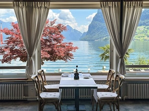 A dining area with a table set for four, facing a large window with a view of a lake and mountains. - Seehotel Kastanienbaum (Horw)