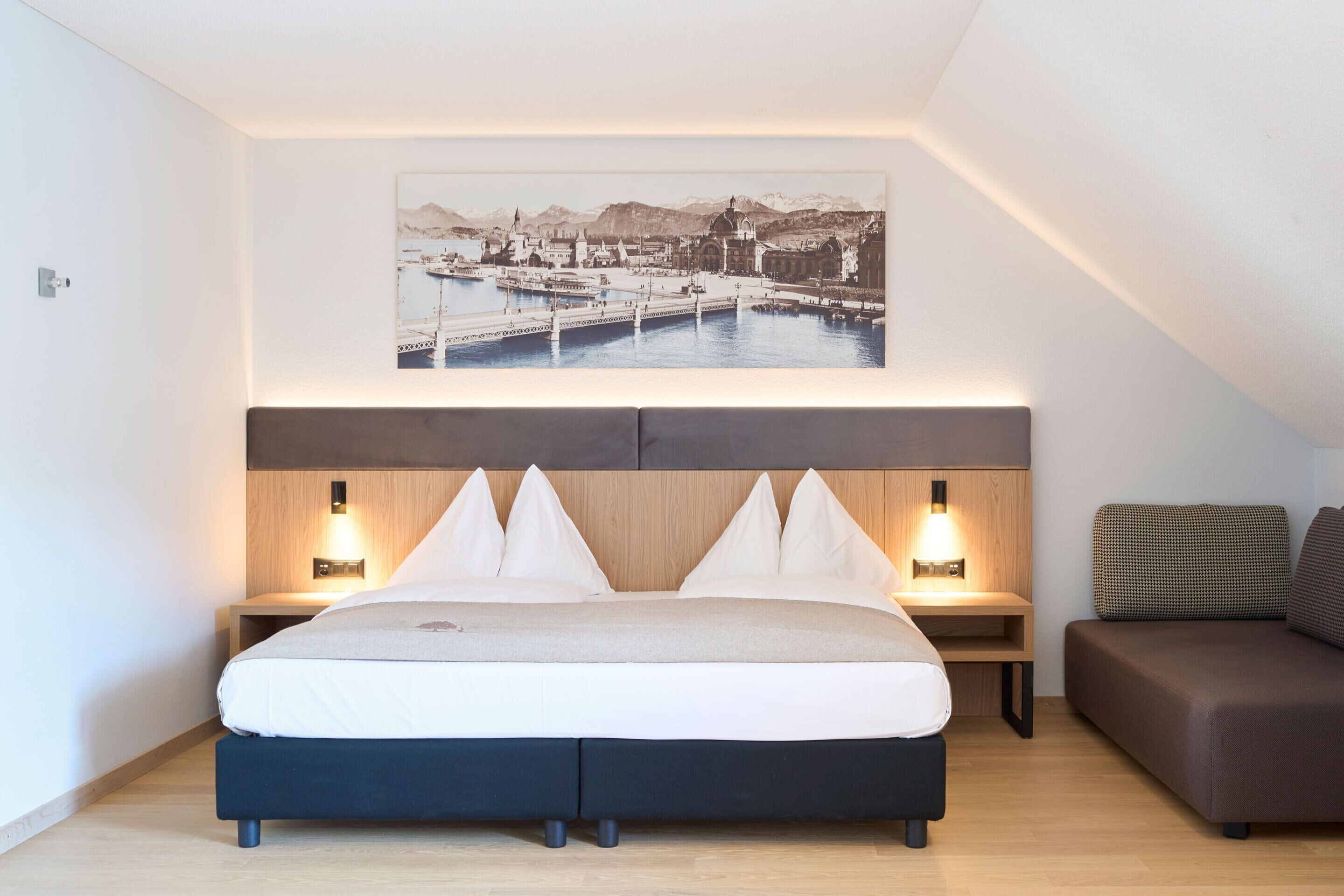 Une chambre d’hôtel avec un lit, des tables de chevet, un canapé et un tableau représentant un paysage urbain accroché au mur.