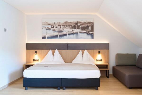 A hotel room with a bed, bedside tables, a sofa, and a cityscape painting on the wall. - Seehotel Kastanienbaum (Horw)